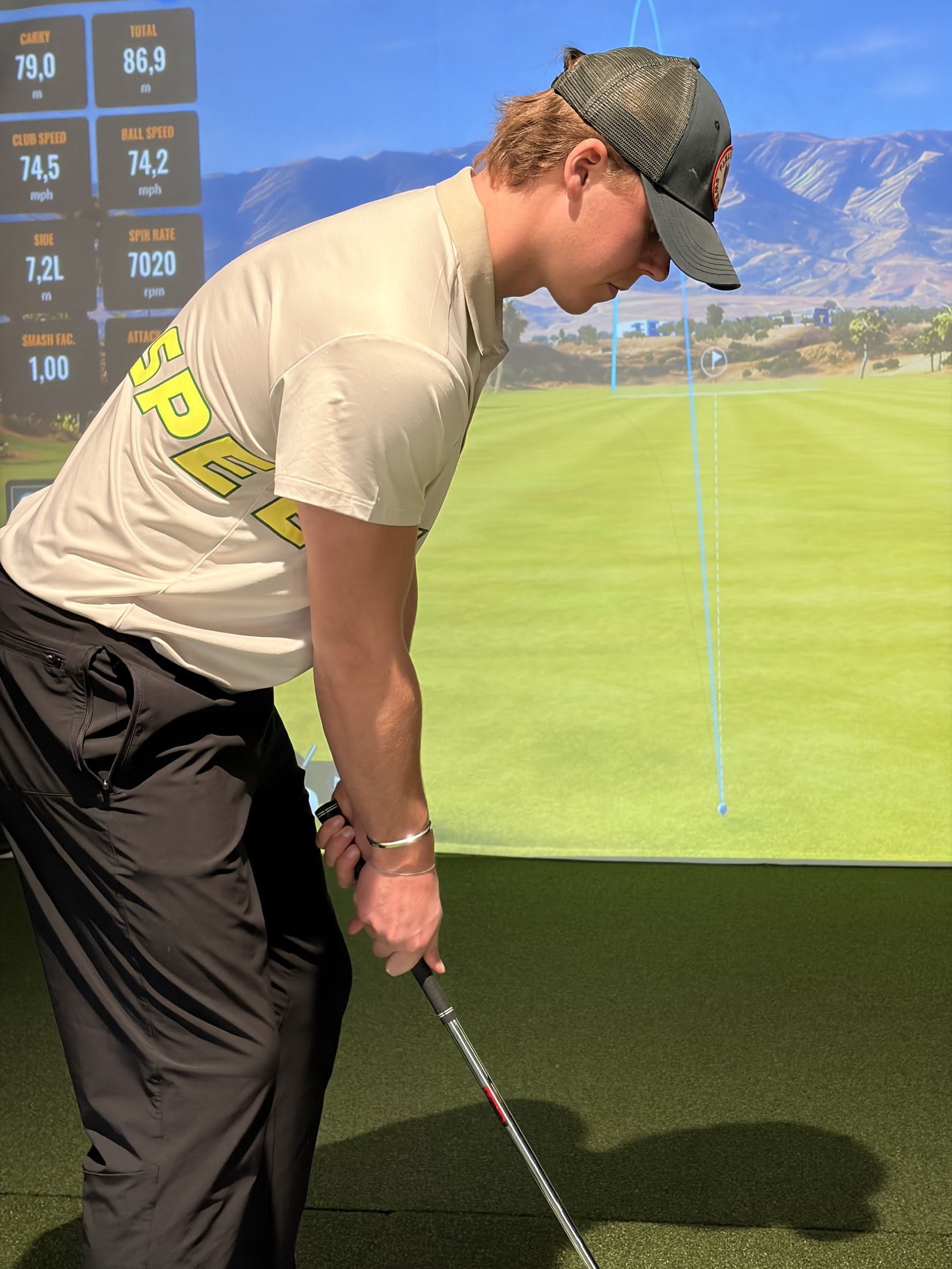 Close detail of the SPEEDY polo side wordmark during an indoor golf setup