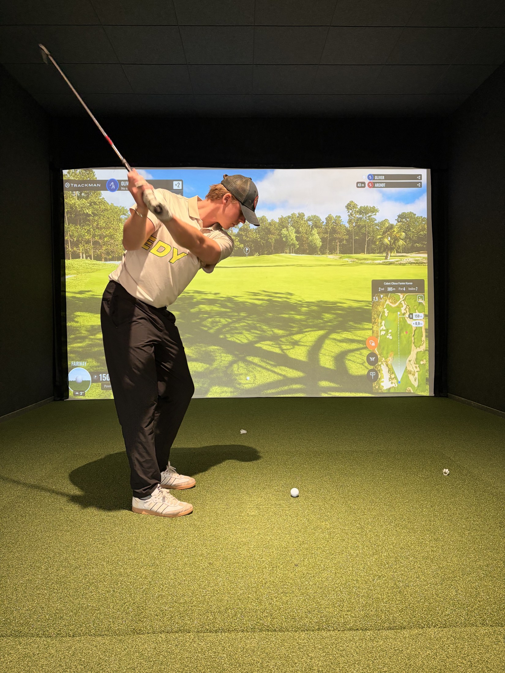 Athlete in a SPEEDY polo finishing a swing in an indoor golf simulator